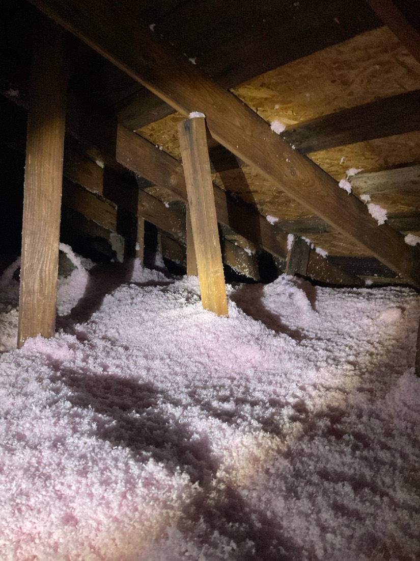 Blown-in pink insulation covering attic floor between wooden framing in residential attic.