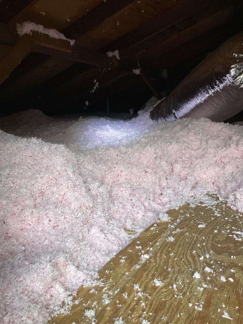 Pink fiberglass insulation batts installed in attic space over existing insulation