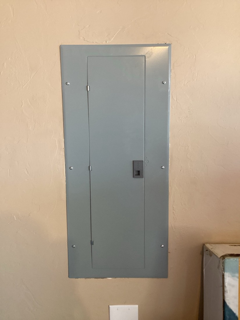 Newly installed gray electrical service panel on interior wall.