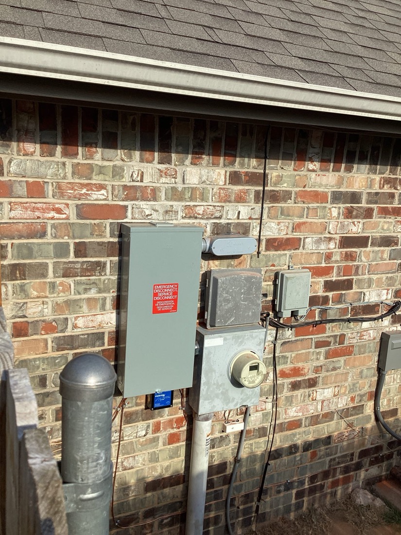 Gray electrical panel with disconnects mounted on brick exterior wall.