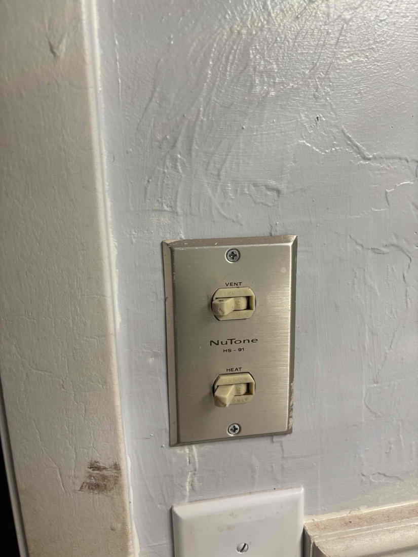 Brushed metal NuTone heat and vent switch on white wall