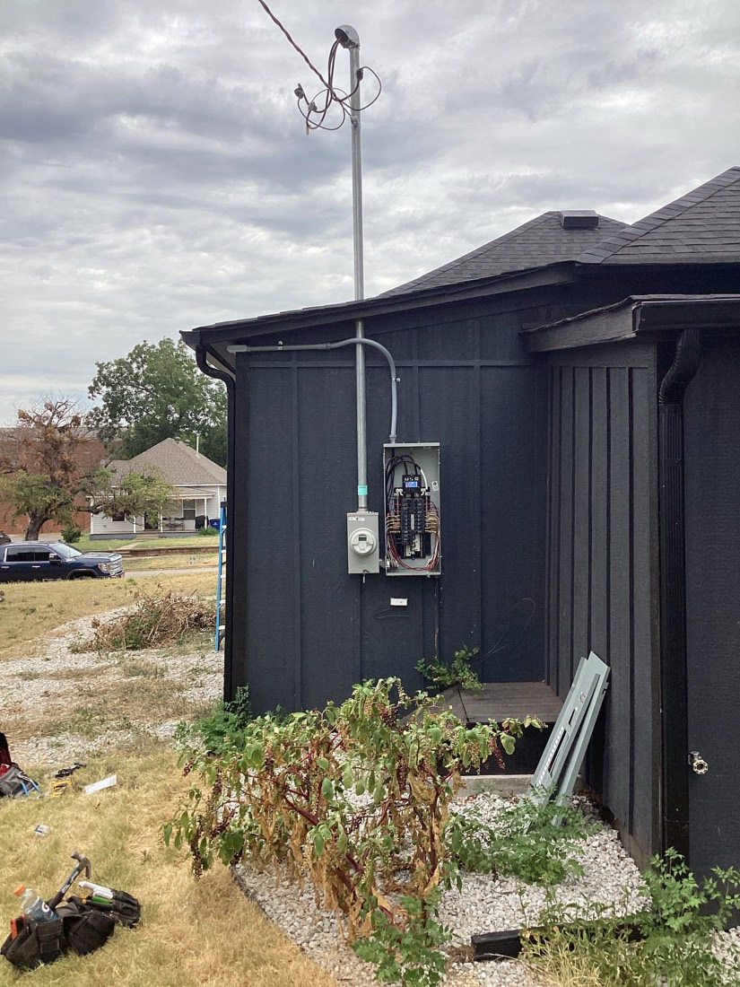 Installed electrical service meter and conduit on dark building exterior.