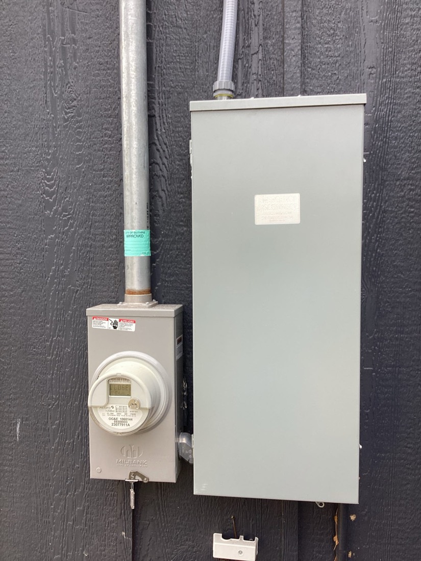 Installed gas meter and white electrical service panel on exterior wall.