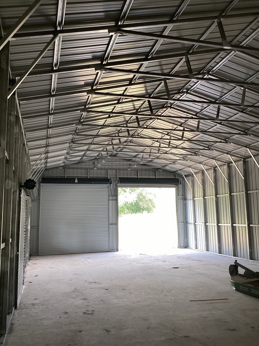 Metal building interior with white garage doors and clear ceiling framing.