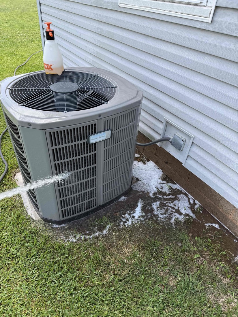 AC unit installed against house exterior with cleaning supplies