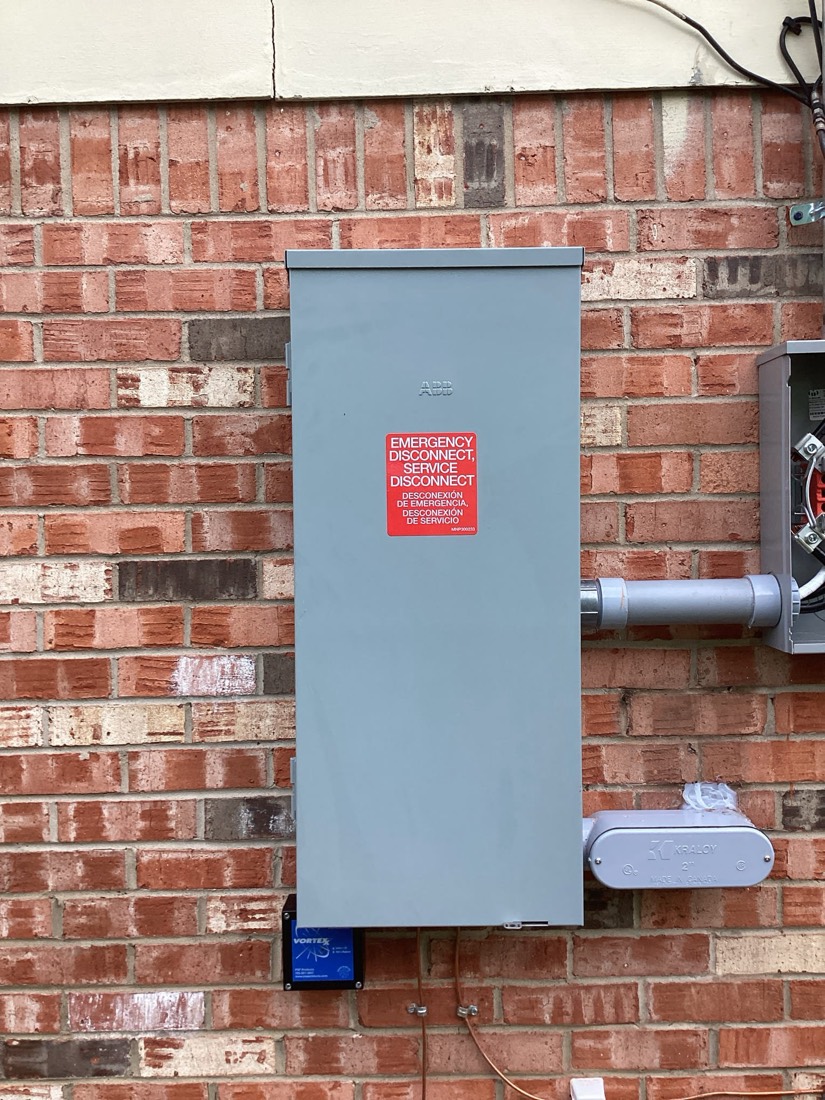 Blue electrical disconnect switch mounted on brick exterior wall.