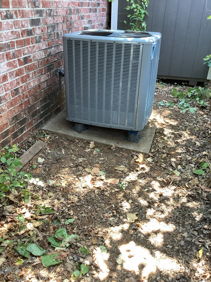 Newly installed air conditioning unit mounted on concrete pad beside brick wall