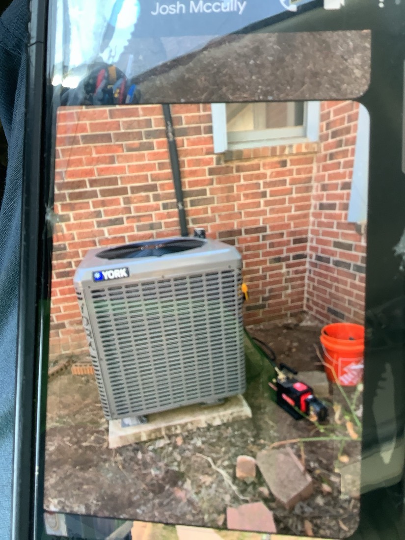 York brand AC condenser unit installed on ground with copper tubing connections and service gauges visible.
