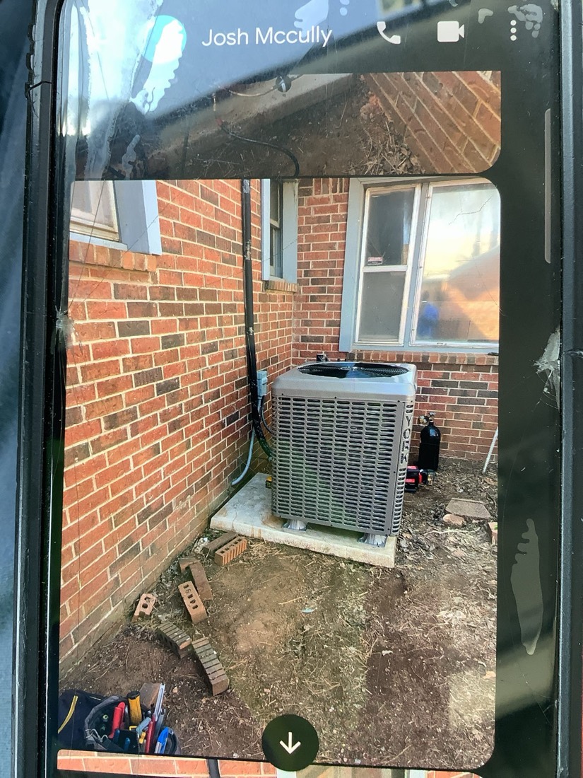 Gray HVAC condenser unit mounted on concrete pad with black copper refrigerant lines connected.