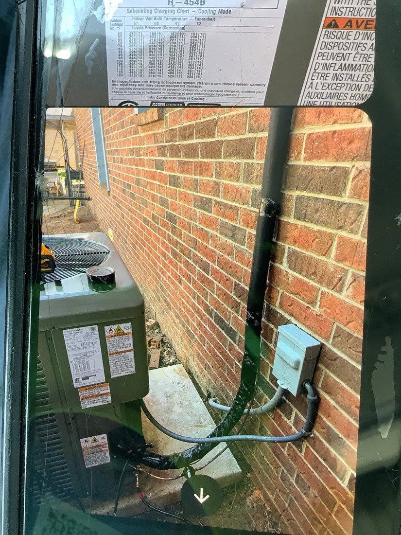 York AC condenser unit installed on concrete foundation beside red brick wall with mounting hardware visible.