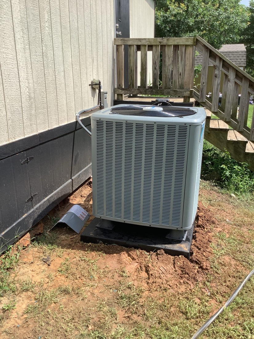 Installed AC condenser unit on mounting pad beside residential deck