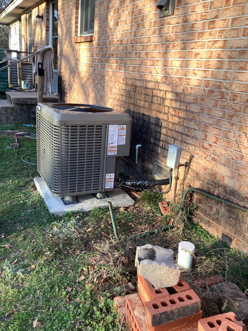 Installed air conditioning condenser unit on concrete pad against brick foundation.