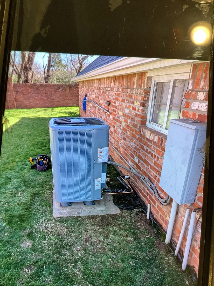 Two new AC condenser units on concrete pads against brick home.
