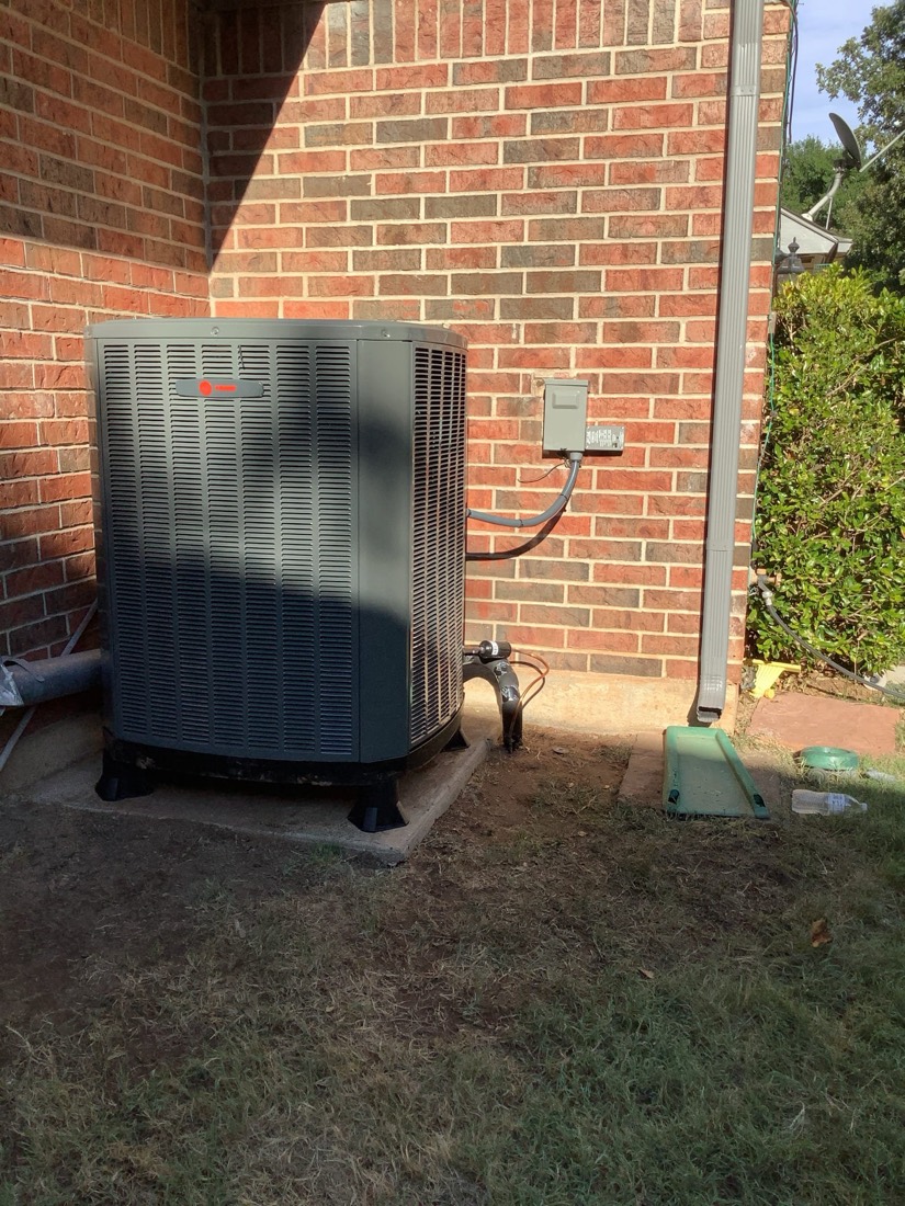 New air conditioner unit mounted on brick exterior with electrical connection.