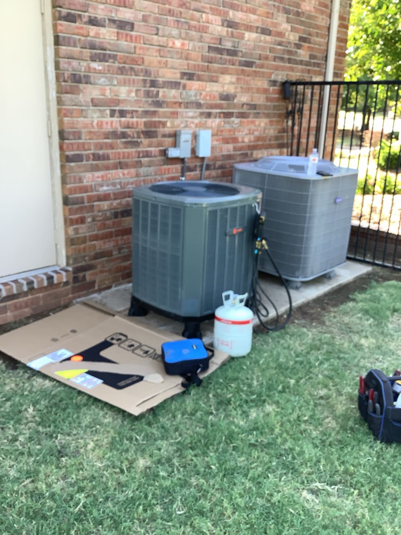 Two AC condenser units installed side by side against brick wall.
