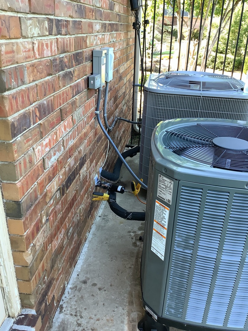 AC condenser unit installed against brick wall with wiring.