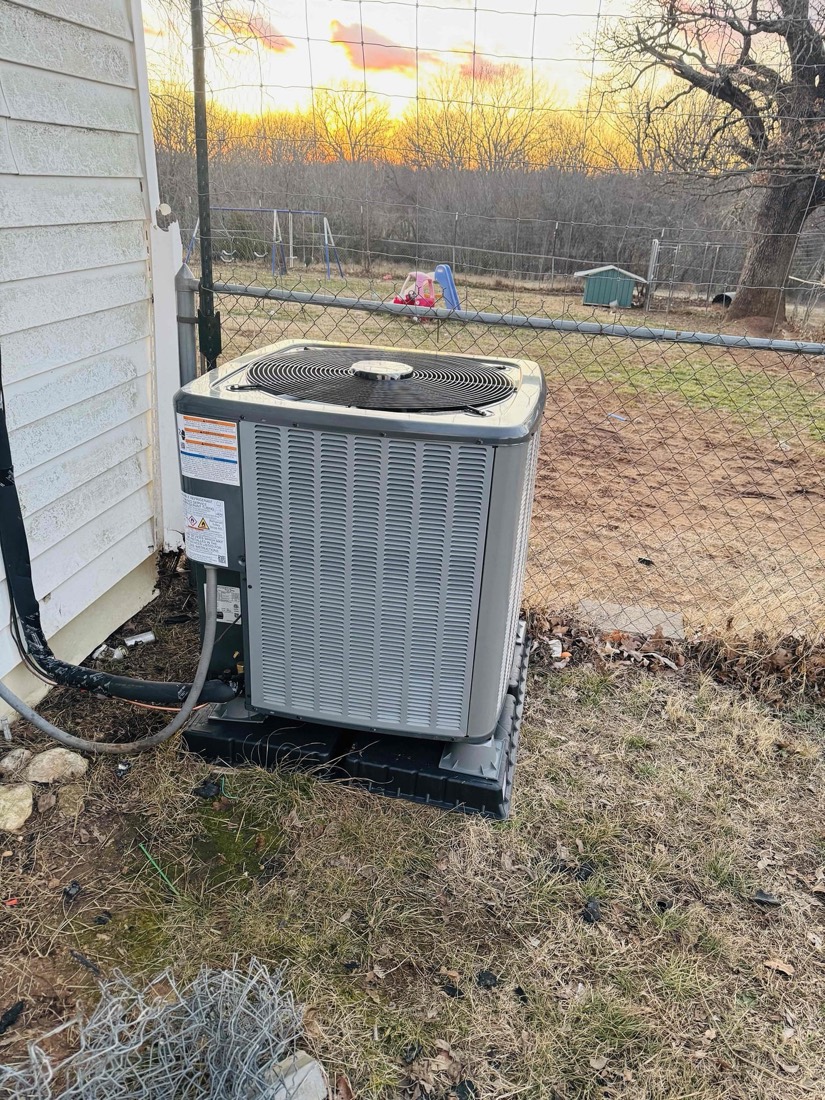 Newly installed gray AC condenser unit on pad next to home.