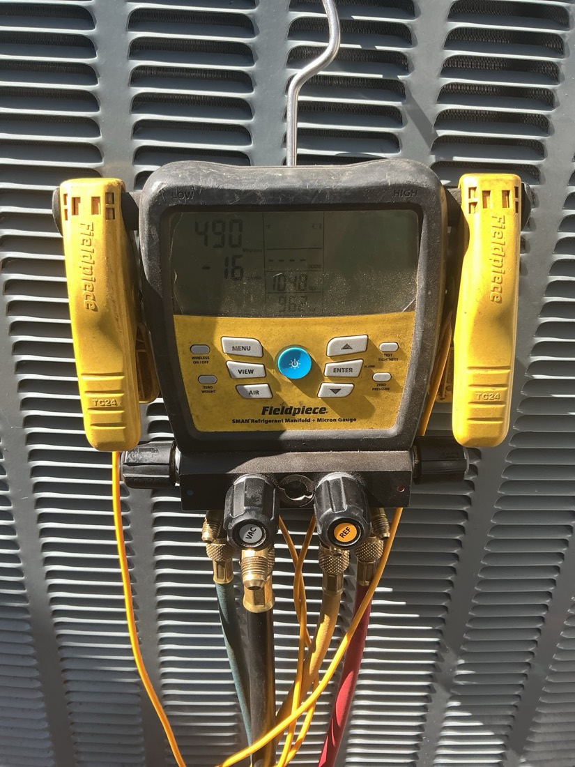 Fieldpiece dual thermometer manifold gauge measuring AC system pressures on evaporator coil.