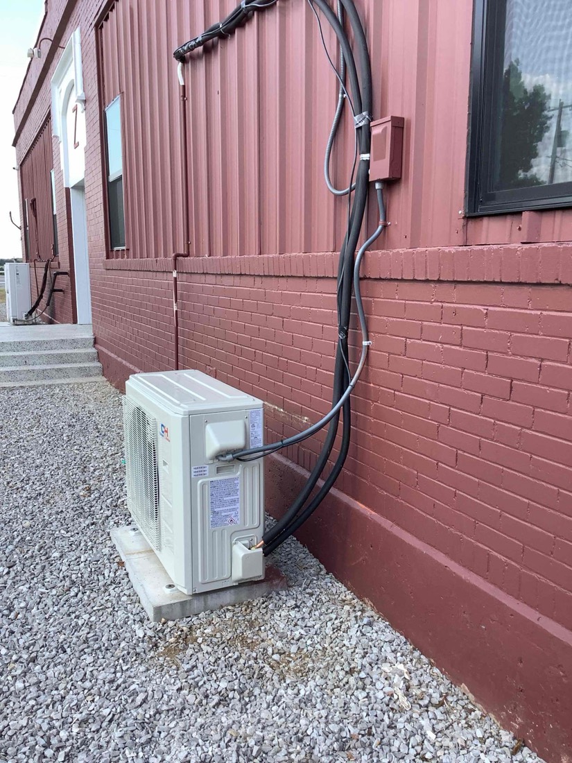 Outdoor mini-split air conditioning unit mounted on concrete pad with refrigerant lines running up building wall